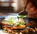 Chef drizzling a green sauce over a finely plated dish with mussels and fresh herbs – sustainable cuisine at Sunstar Hotel.