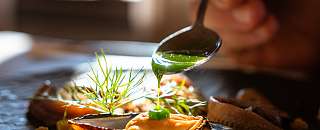 Chef drizzling a green sauce over a finely plated dish with mussels and fresh herbs – sustainable cuisine at Sunstar Hotel.